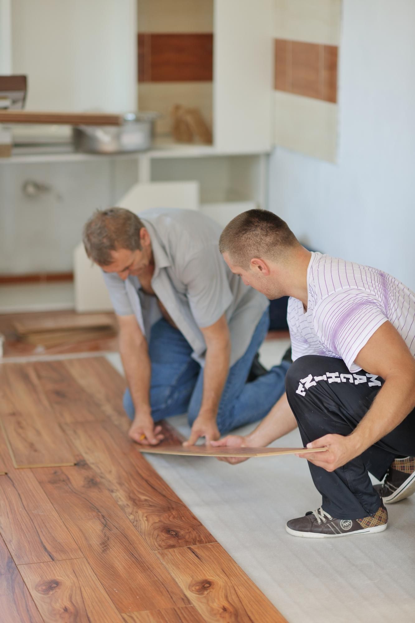 Dos carpinteros colocan un suelo laminado de madera en un piso.