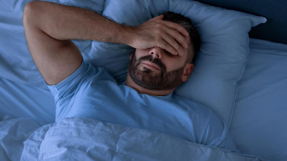 Un hombre que padece insomnio se cubre el rostro con la mano.