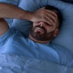 Un hombre que padece insomnio se cubre el rostro con la mano.