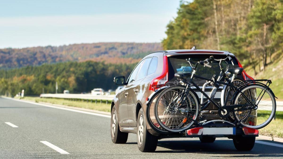 Un coche circula por una autopista con dos bicicletas cargadas en su portón trasero.
