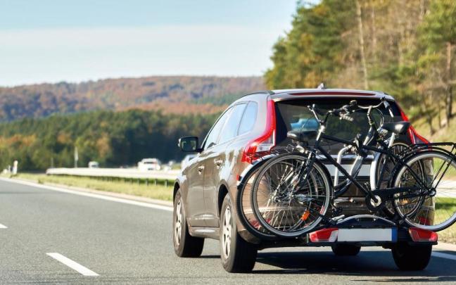 Un coche circula por una autopista con dos bicicletas cargadas en su portón trasero.