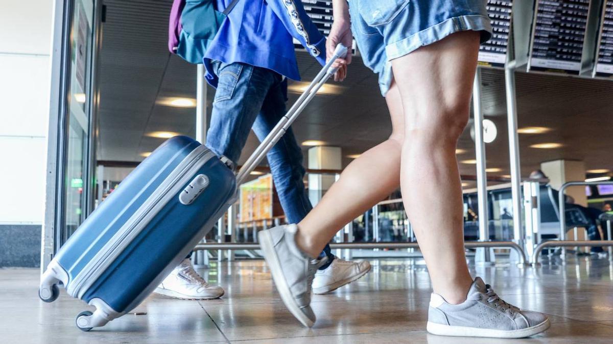 Dos viajeros con maletas de mano en el aeropuerto.