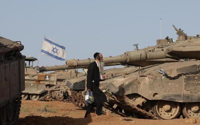 Un hombre pasea entre vehículos israelías blindados asentados en junto a la frontera de Gaza.