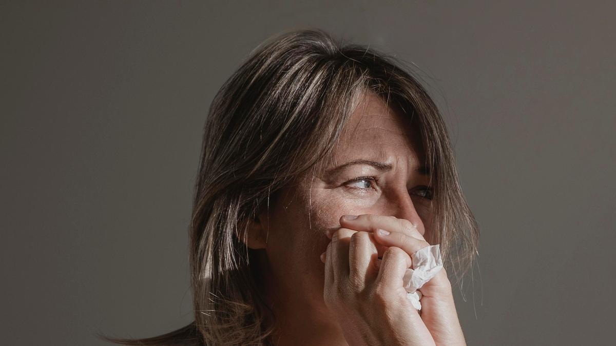 Una mujer sujeta un pañuelo entre sus manos para secarse las lágrimas.