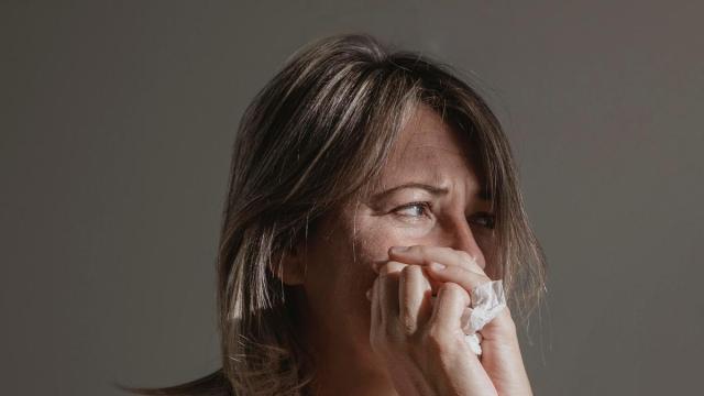 Una mujer sujeta un pañuelo entre sus manos para secarse las lágrimas.