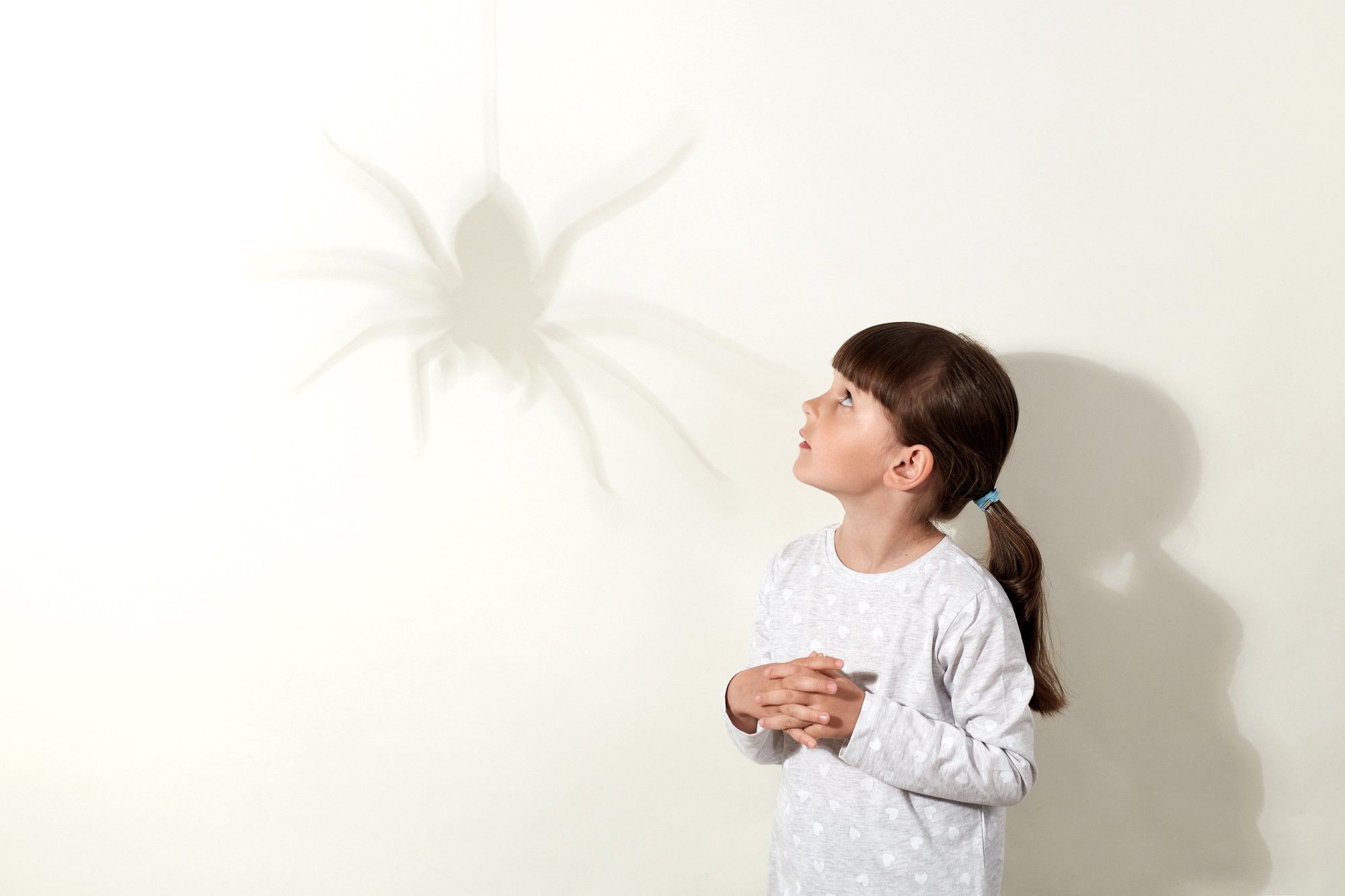 Una niña mira con temor la sombra de una araña proyectada en la pared.