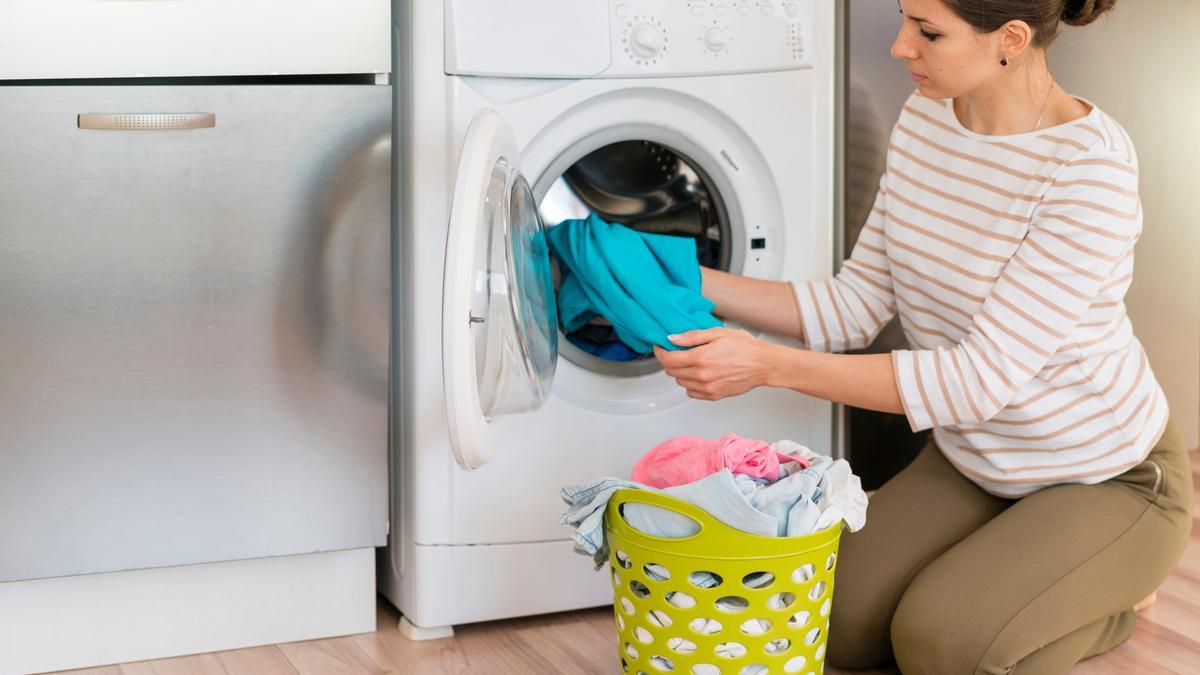 Una mujer mete la ropa en la lavadora