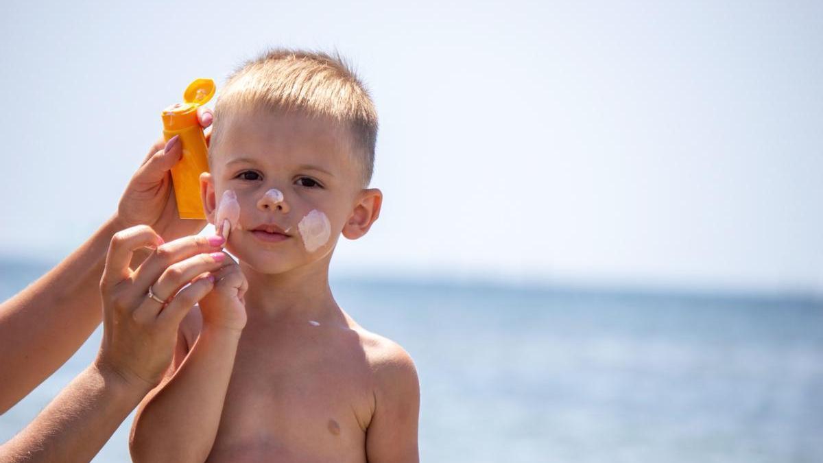 Madre aplica protector solar a su hijo en la playa.