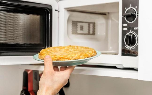 Un hombre mete una tortilla de patatas al microondas para calentarla.