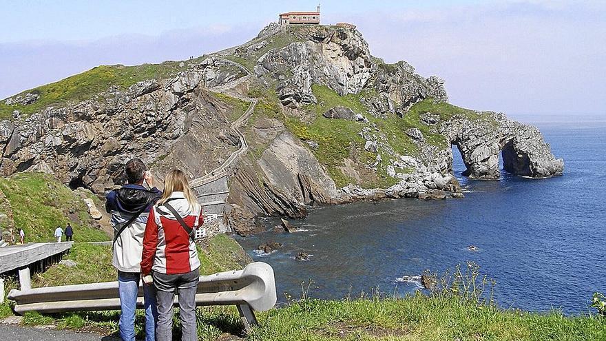 Dos turistas toman fotografías al islote de San Juan de Gaztelugatxe
