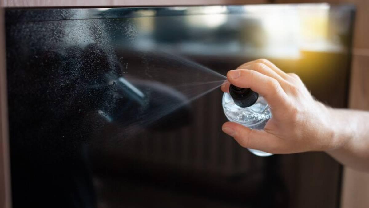 Mano de un hombre limpiando la televisión con un producto de limpieza en spray