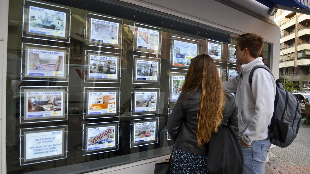 Dos jóvenes ajenos a esta información buscan piso de alquiler en un escaparate.