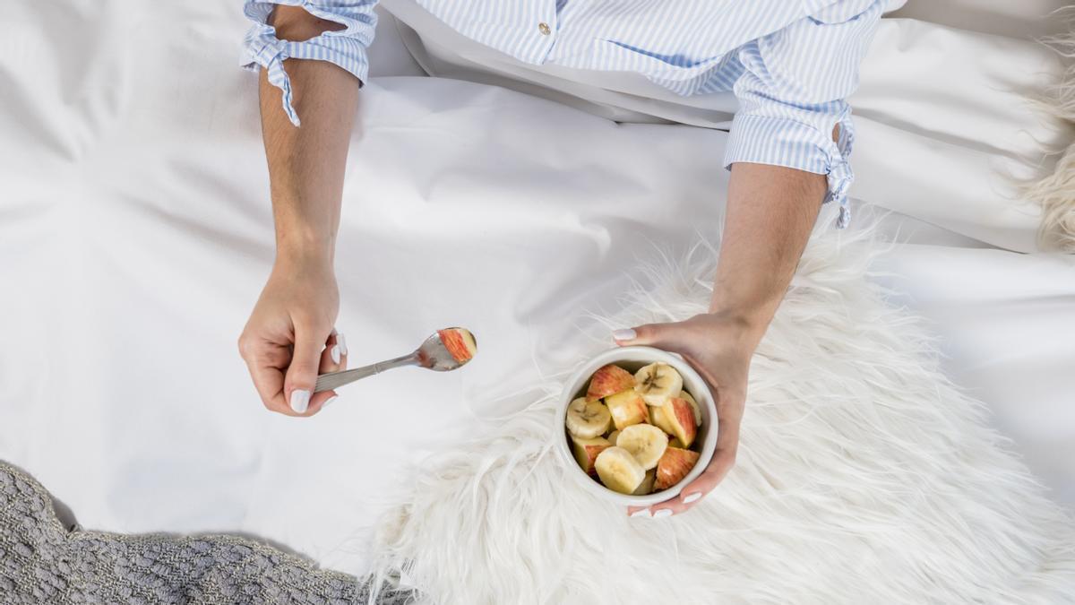 Manos de una mujer tomando un bol de fruta con plátano y manzana antes de dormir.