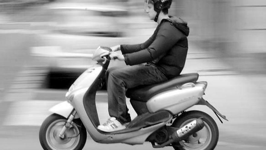 Un joven conduce un ciclomotor por la calzada.