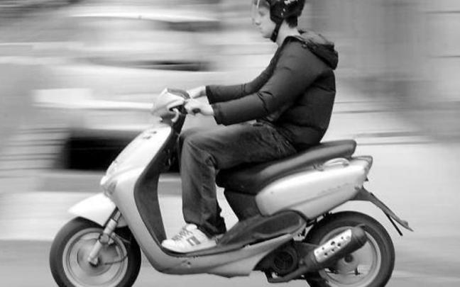 Un joven conduce un ciclomotor por la calzada.