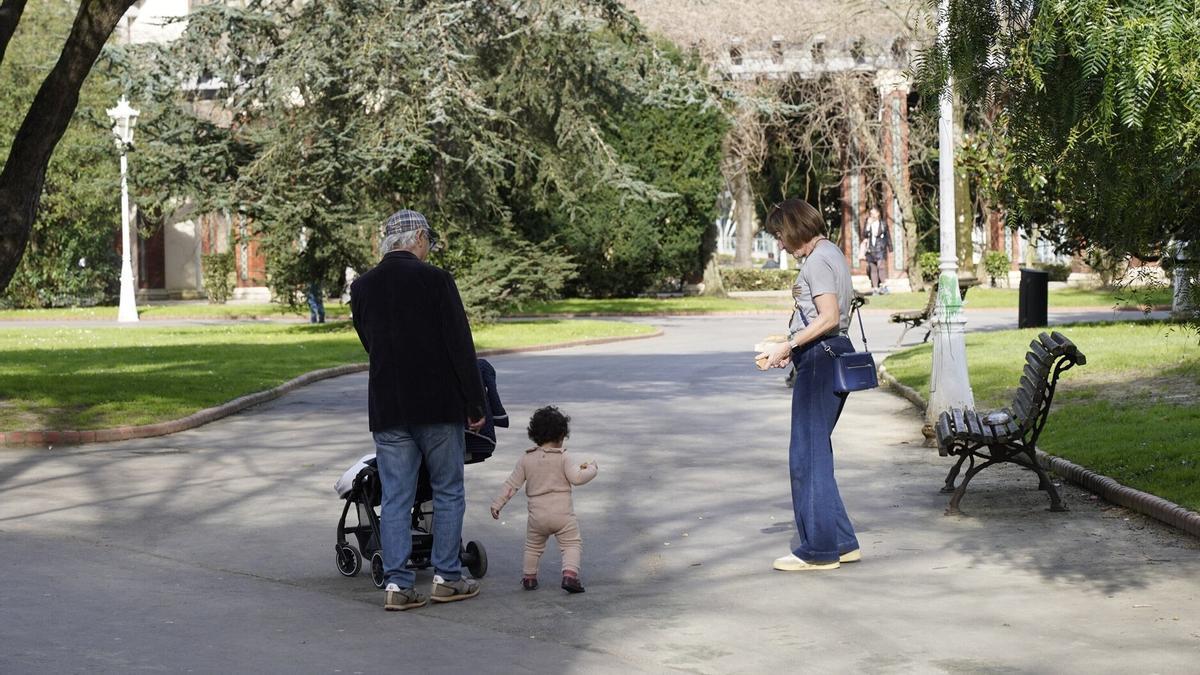 Dos personas mayores disfrutan de un paseo por el parque en compañía de su nieta.