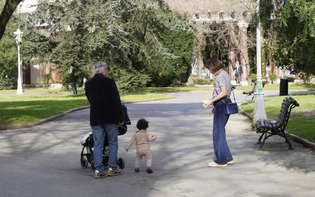 Dos personas mayores disfrutan de un paseo por el parque en compañía de su nieta.