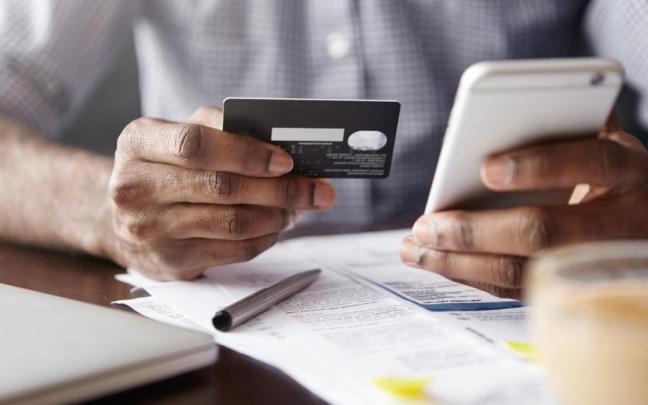 Un hombre realiza un pago a través del móvil con una tarjeta bancaria.