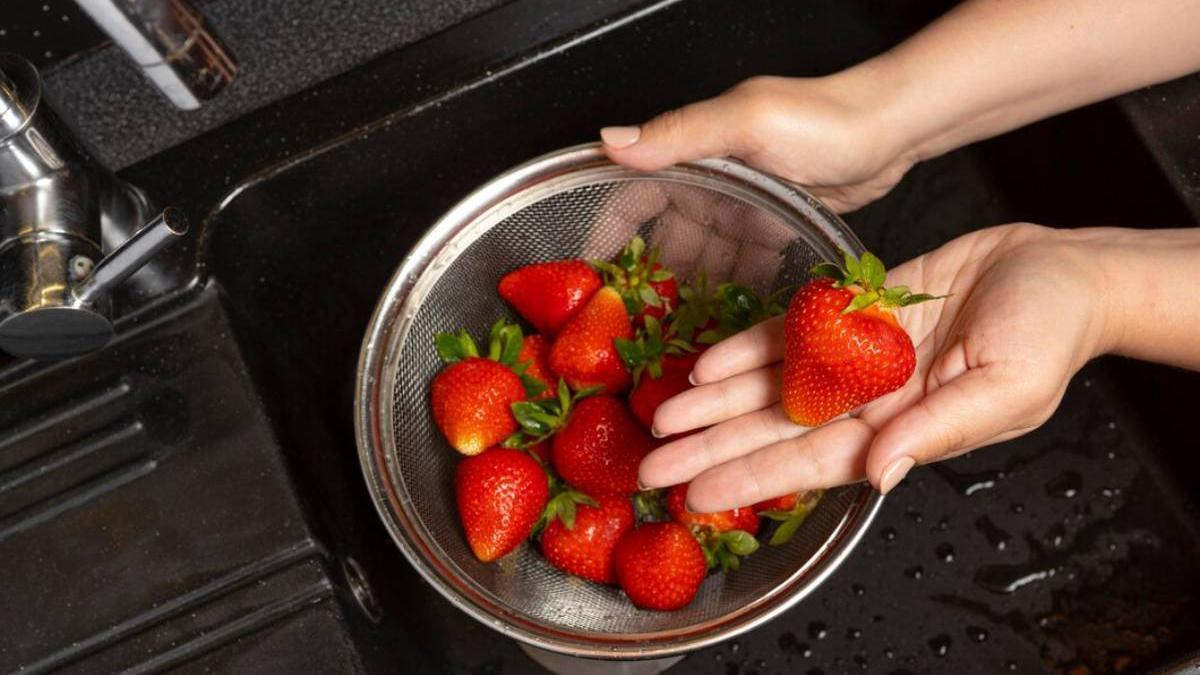 Manos de una chica lavando unas fresas en el fregadero con ayuda de un colador.