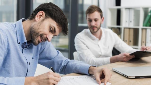 Un hombre firma la contratación de un seguro ante la mirada de un agente.