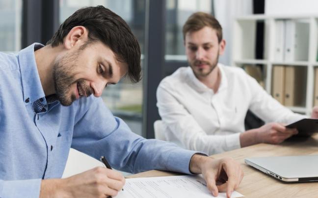 Un hombre firma la contratación de un seguro ante la mirada de un agente.