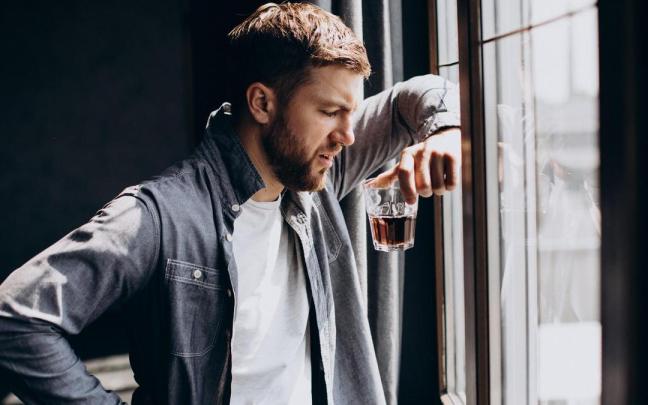Un hombre sujeta un vaso apoyado en una ventana.