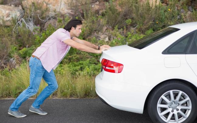 Un hombre empuja su coche tras quedase sin batería.