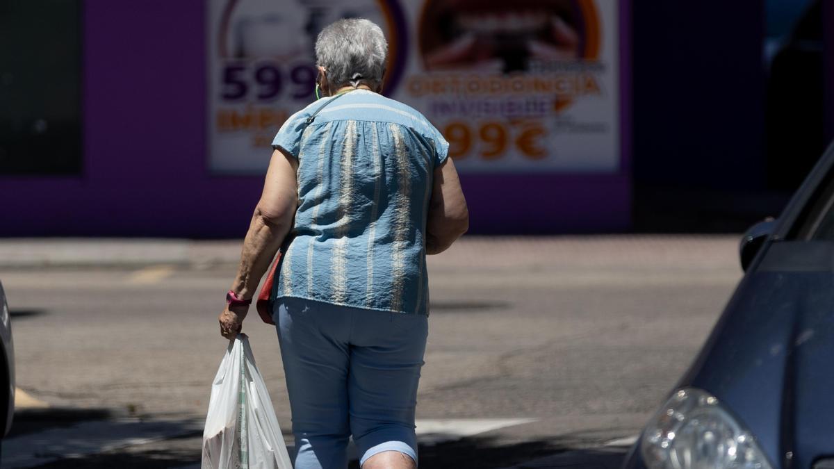 Imagen de una señora mayor sujetando una bolsa mientras camina.