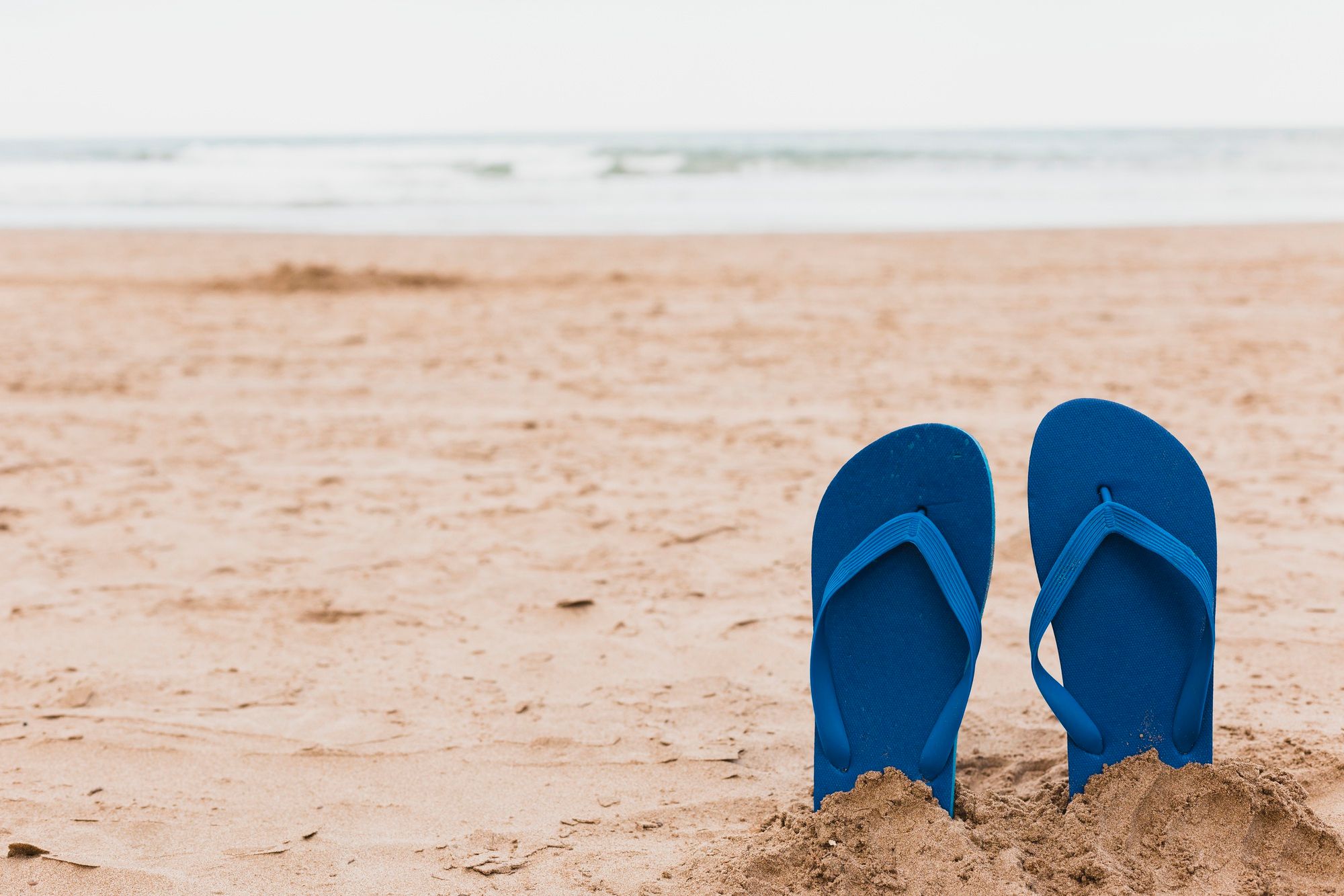 Un par de chancletas de plástico clavadas en la arena de la playa.