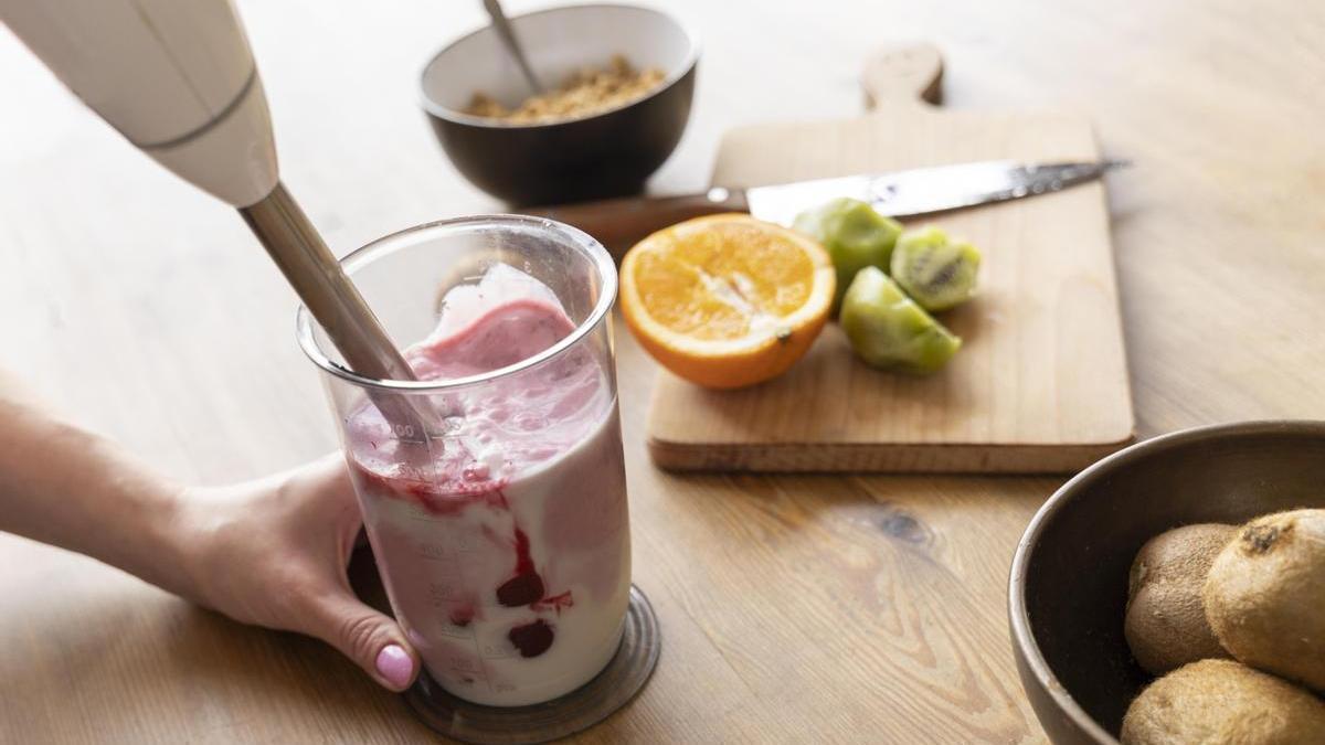 Manos preparando un batido saludable casero de fruta con ayuda de una batidora