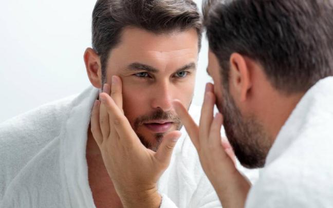 Hombre observa su rostro frente al espejo para comprobar el estado de su piel.