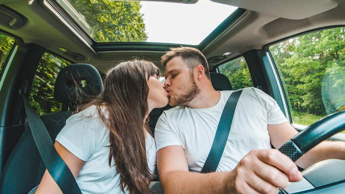 Un conductor y su acompañante se besan en el interior de un coche mientras él conduce.