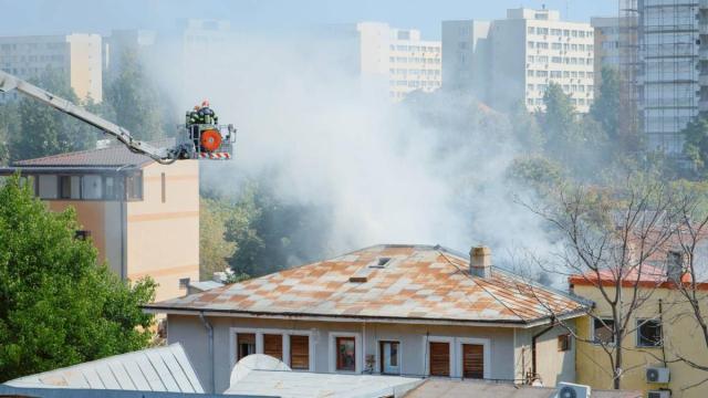 Unos bomberos sobre una grúa tratan de apagar un incendio originado en una vivienda