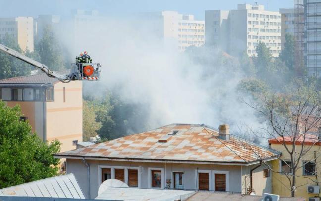Unos bomberos sobre una grúa tratan de apagar un incendio originado en una vivienda