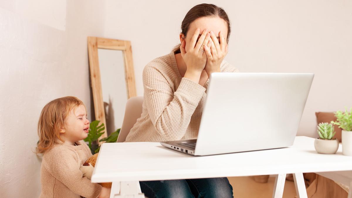 Una mujer teletrabaja mientras su hija pequeña la reclama.