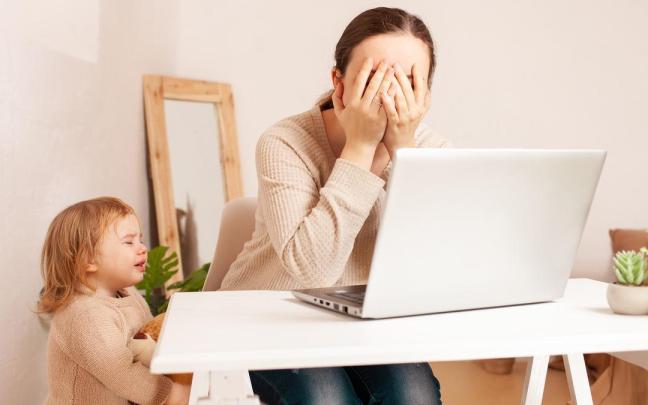 Una mujer teletrabaja mientras su hija pequeña la reclama.
