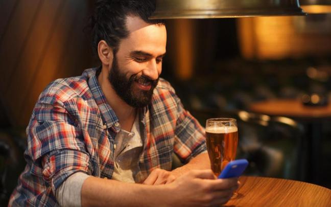 Un hombre interactúa con un personaje virtual a través de su móvil en un bar.