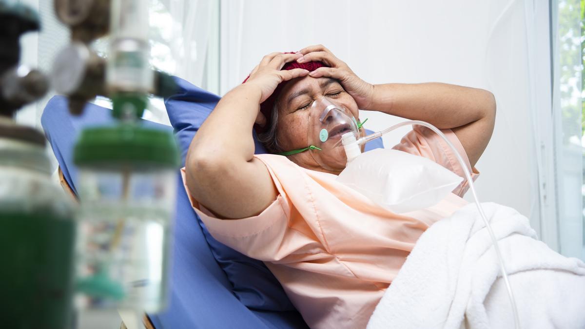 Una mujer se lleva las manos a la cabeza mientras permanece postrada en la cama del hospital, en un gesto de dolor y abatimiento.