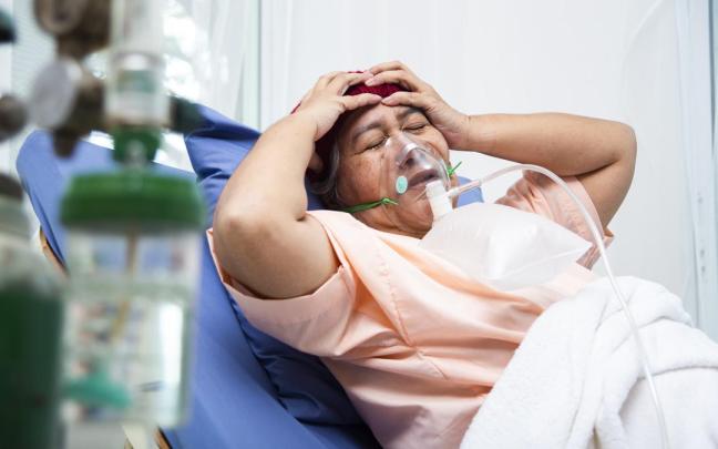 Una mujer se lleva las manos a la cabeza mientras permanece postrada en la cama del hospital, en un gesto de dolor y abatimiento.