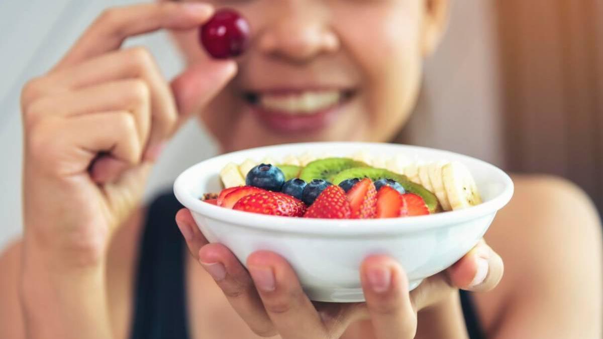 Joven sonriente disfruta de un bol de frutas variadas