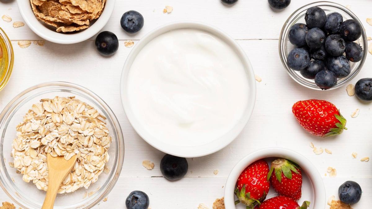 Tazón de yogur griego rodeado de frutas y cereales.