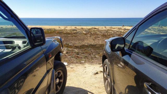 Dos coches aparcados frente a una playa.