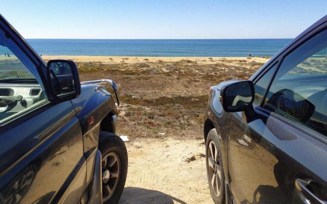 Dos coches aparcados frente a una playa.