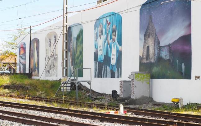 El mural, pintado en la fachada posterior del Paseo Cubierto, recibe a los viajeros que llegan en tren a Deba.