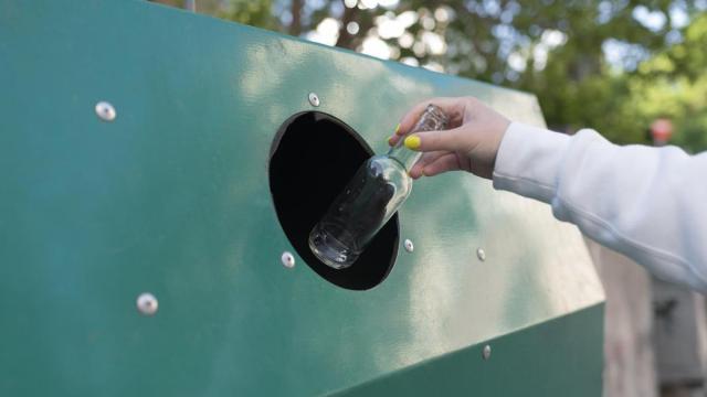 Una mujer tira una botella en un contenedor de reciclaje.