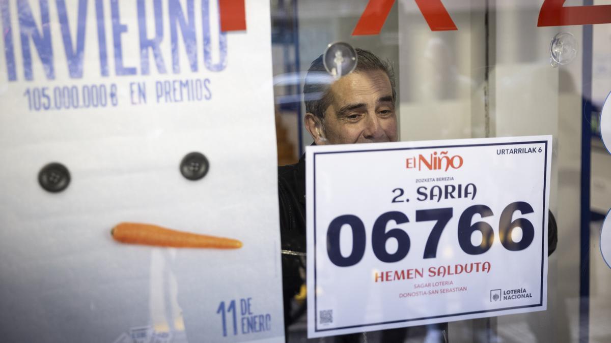 Dueño de una administración de lotería coloca un cartel en el cristal con el número premiado