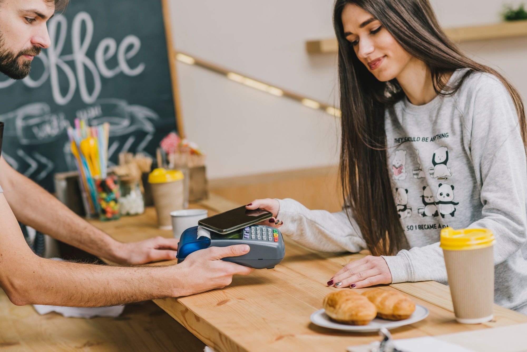 Una mujer joven paga el desayuno con el teléfono móvil en una cafetería.