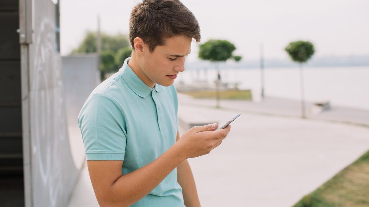 Un chico joven lee un mensaje en su teléfono móvil.