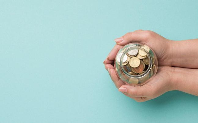 Unas manos sujetan un tarro de cristal con monedas de euro. Unas manos sujetan un tarro de cristal con monedas de euro.