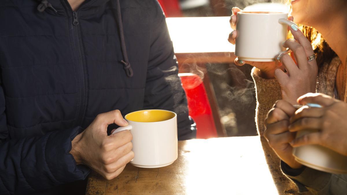 Grupo de personas disfrutan de una bebida caliente en la terraza de un bar mientras sonríen y mantienen una conversación agradable